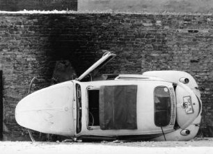 Auf die Seite gekippter VW-Käfer vor einer Hinterhofwand