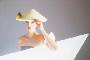 Model in Schaumstoffmode : Model mit gelbem Schaumstoffhut hinter einem Neonleuchtkörper