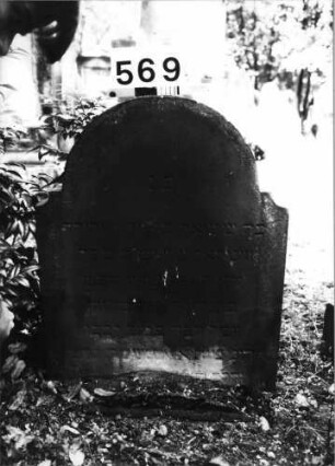 Grabstein 569 (Index: 99630070) Material: Sandstein Zustand: eingesunken, abgeblättert/Textverlust Maße HxBxT: 79x59x7 cm Beschreibung: Stele mit eingezogenem Runbdogenabschluß: Grabstein 569