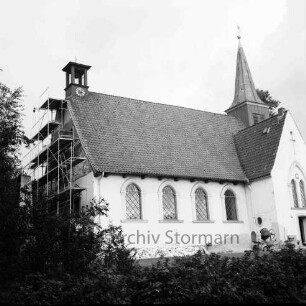 Matthias-Claudius-Kirche: Paul-von-Schoenaich-Straße: Renovierung: Außenaufnahme: Blick von Südwesten: Erneuerung des Außenputzes an westlicher Giebelwand, Gerüst, Zementmischmaschine: im Vordergrund Hecke