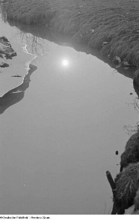 Ein vereister Bachlauf mit sich spiegelnder Sonne