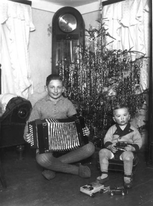 Zwei Jungen mit Ziehharmonika und Spielzeug vor einem Weihnachtsbaum