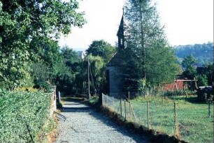 unbefestigter Weg zwischen Gärten, hinten rechts Glockenhäuschen