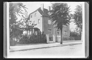 Haus mit Zaun, davor Straße und Bäume