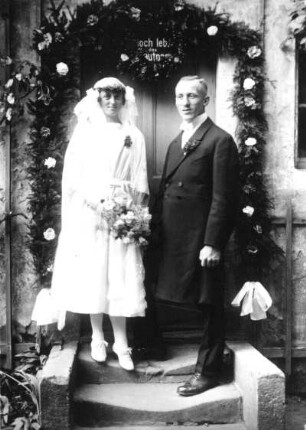 Hochzeitspaar vor mit Spruch und Girlanden geschmückter Tür