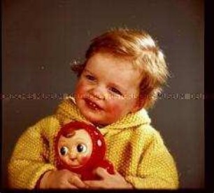 Kleines Mädchen mit Strickjacke und Puppe