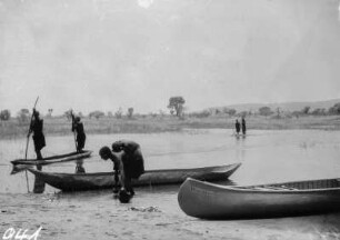 Am Fluss : Personen mit Kanu und Einbäumen an einem Flussufer