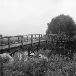 Trave: Holzbrücke "Grüne Brücke": rechts darauf Fußgänger vorn Gesträuch: hinten rechts Bäume