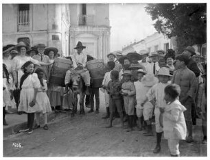 Puerto Cabello (Venezuela). Einheimische, Kinder und Touristen gruppieren sich um einen Lastesel mit zwei hölzernen Fässern