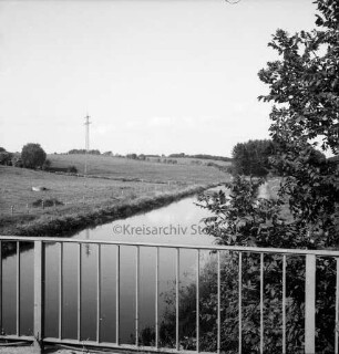 Trave: Blick von der Brücke auf Travetal mit angrenzender Knicklandschaft: rechts Büsche: hinten links Strommast der Überlandleitung auf Weide
