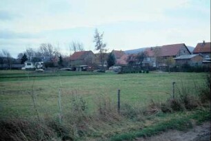 Dorfrand mit Wiese, Weidezaun, dahinter Gebäude