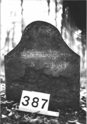 Grabstein 387 (Index: 99898331) Material: Sandstein Zustand: fast völlig verwittert Maße HxBxT: 58x46x6 cm Beschreibung: Stele mit überhöhtem Konvexbogenabschluss Besonderheit: Identifizierung nach Gräberverzeichnis: Grabstein 387