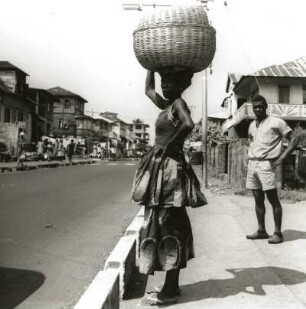 Freetown, Sierra Leone. Straßenszene am Rande der Stadt mit Afrikanerin, eine Last auf dem Kopf tragend. Blick gegen die Sierra Leone