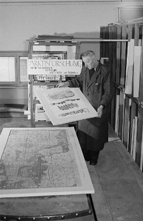 Mitarbeiter bei Betrachten von Karten im Institut für Länderkunde in Leipzig, am Regal ein Plakat mit der Aufschrift " Die Arktisforschung ist für Wissenschaft, Wirtschaft und Verkehr von Bedeutung"