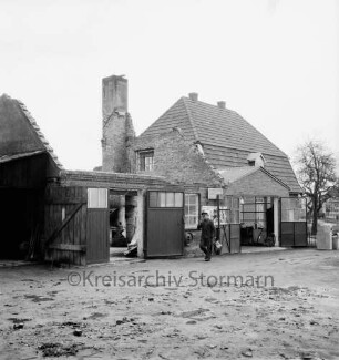 Huf- und Wagenschmiede: Brandruine mit Schornstein: davor Mann: dahinter Wohnhaus: vorn Sandfläche mit Schutt