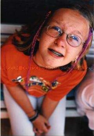 Mädchen mit Brille, Zahnspange und bunten Zöpfen schaut nach oben (Altersgruppe bis 14)