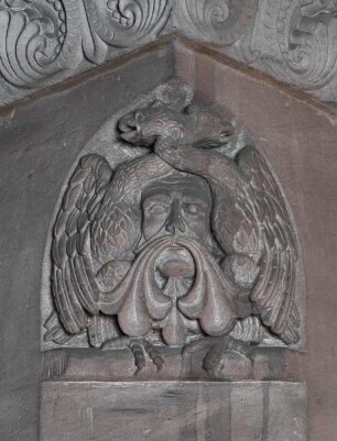 Zwickelrelief mit zwei Drachen und einem Gesicht unter dem Kämpfer