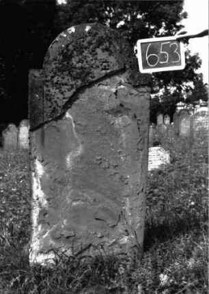 Grabstein 653 (Index: 100104939) Material: Sandstein Zustand: stark verwittert, abgeblättert, fast vollständiger Textverlust Maße HxBxT: 151x66x10 cm Beschreibung: Stele, eingezogener Rundbogenabschluss, Schriftfeld eingetieft mit Konvexbogenabschluss: Grabstein 653
