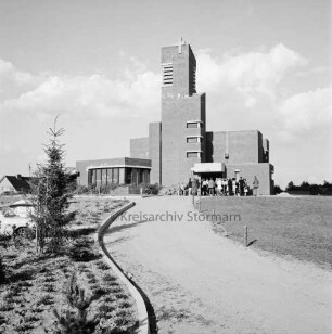 Evangelische Kirche: vorn Mitte Sandweg: rechts und links davon teilweise Grünanlagen mit Zaun: hinten rechts vor Eingang Menschenmenge: hinten links Sandhaufen