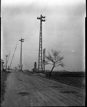 Deutschland. Erste 110 kV-Freileitung des Elektroarmaturenwerks Radebeul-Kötzschenbroda). Leitungsmasten an einer Landstraße. Blick gegen beschrankten Bahnübergang und Fahrleitungsmast