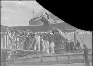 Vier Matrosen und weitere Besatzungsmitglieder vor der Katapultbahn, auf der ein Postflugzeug befestigt ist, Hochseepassagierdampfer "Bremen"