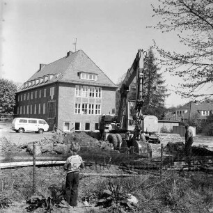 Woldenhorn-Schule: Sonderschule des Kreises Stormarn für geistig behinderte Kinder: Ecke Reeshoop / Schulstraße: Erweiterungsbau: in Bau: Bagger bei Ausheben der Baugrube: Arbeiter, Aushub, Eisenträger, Bretter, Bauwagen, Kleintransporter: hinten Altbau: Blick von Hans-Schadendorff-Stieg aus: im Vordergrund Kind bei Blick durch Maschendrahtzaun