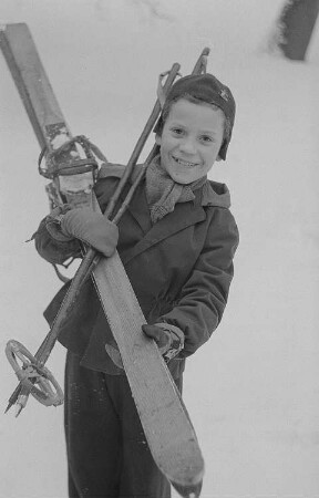 Kinder beim Ski- und Schlittenfahren, Junge mit Ski nach der Abfahrt
