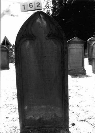 Grabstein 162 (Index: 99798012) Material: Sandstein, rot Zustand: leicht verwittert Maße HxBxT: 142x60x17 cm Beschreibung: Stele, Spitzbogenabschluß Symbolik: Maßwerk: Grabstein 162