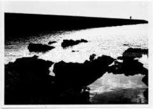 Umrisse von zwei Personen, die auf einem Damm am Wasser laufen (Altersgruppe 18-21)