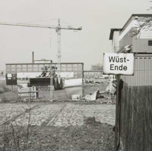 Kreuzung einer Werkstraße mit einem Anschlußgleis und Schild 'Wüst-Ende' (Wagenübergabestelle) gegen eine Baustelle