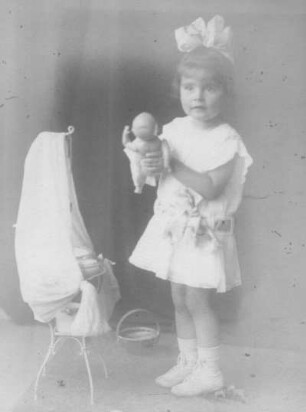 Album mit Porträtserie eines kleinen Mädchens. Mädchen im Sommerkleid, neben einem Puppenbett stehend und eine Puppe haltend