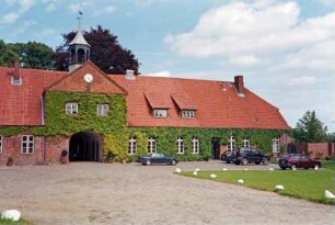 Altfresenburg: Gut: Torhaus, Teilansicht: Blick von Westen: Mittelteil mit Torduchfahrt, Zwerchhaus, in Giebel Uhr, darüber Dachreiter: rechter Gebäudeteil mit Sprossenfenstern, Tür: Kletterpflanzen