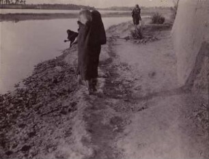 Euphrat bei Babylon : Frau mit Wasserkrug auf der Schulter am Ufer des Euphrat. Daneben eine weitere Frau mit Gefäß.
