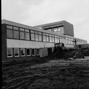Hauptschule mit Realschulzug [später Joachim-Mähl-Schule]: Schulverband Reinfeld: Schützenstraße: nach Fertigstellung: Herrichten des Außengeländes: neben Schulgebäude Betonmauern, Erdhaufen, darauf Laderaupe, zwei Arbeiter