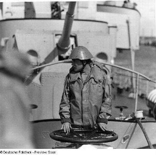 Deutschland . Nationale Volksarmee - Seestreitkräfte. Matrose im Kampfanzug-See mit Stahlhelm an einem Handrad auf Deck, hinter ihm Bordgeschütz