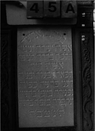 Grabstein 45 (Index: 100086687) Material: Sandstein mit zwei weißen Marmorplatten Zustand: Sandstein teilweise abgeblättert Maße HxBxT: 177x58x24 cm Beschreibung: ädikulaartige Stele mit Pilastern, getreppter Sockel, giebelartiger Abschluß mit Verdachung und Eckakroteren Symbolik: negatives Zahnfries, Mohnkapseln, Blüten, Ranken: Grabstein 45A