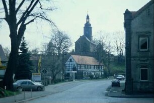 Straßenabschnitt, Gebäude des Zentrums für Handwerk und Denkmalschutz, darüber Dorfkirche