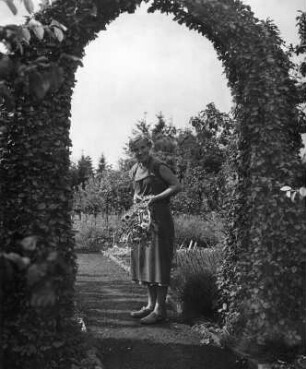 Blumen. Frau mit Blumenstrauß unter einem Heckenbogen