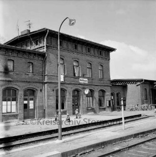 Bahnhof: davor Kinder mit Fahrrädern: im Vordergrund Gleisanlagen und Bahnsteige