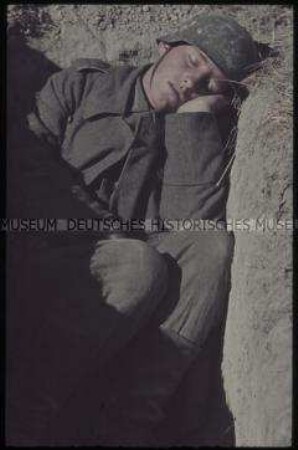 Schlafender deutscher Soldat mit Stahlhelm in einem Panzergraben