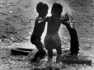 Hamburg-Harburg. Zwei Kinder spielen in einem Wasserbecken eines Kinderspielplatzes. Sie stehen an einer Düse