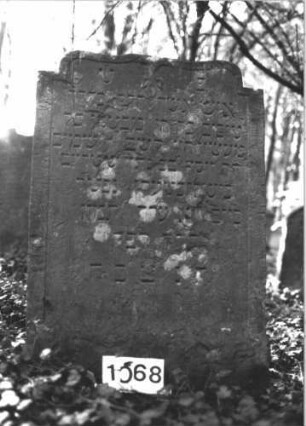 Grabstein 1068 (Index: 99899700) Material: Sandstein Zustand: etwas angewittert Maße HxBxT: 112x74x7 cm Beschreibung: Stele mit flachem Schulterbogenabschluss, von der Spitze herabhängende Blüte Symbolik: Blüte: Grabstein 1068