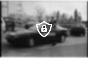 Autohaus Homburg: Hammoorer Weg: Parkplatz: Juniorchef [Name maskiert] an offener Autotür von Testwagen Toyota Celica: hinten Autos, Hüpfburg, Werbefahnen, Straße: 26. März 1990