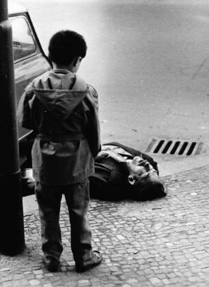 Junge in Betrachtung eines auf der Straße liegenden Mannes