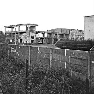 Glinde: Oher Weg: Gelände des ehemaligen Heereszeugamtes: Betonmauer mit Stacheldraht: dahinter Ruine eines Gebäudes: vorn Sträucher