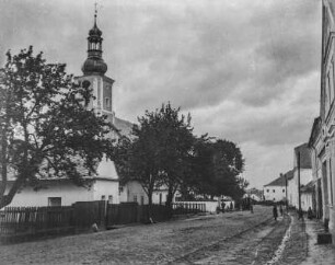 Straßenszene : Blick in eine Dorfstraße. Rechts einige Passanten, in der Mitte Blick auf eine Kirche