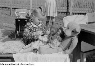 Kleines Mädchen mit Spielzeugpuppen und einem Teddybär