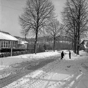 Dorfstraße: links Volksschule mit Vorgarten: rechts zwei Kinder: hinten Bäume und Häuser: Winter