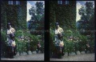 Frau in einem langen Kleid vor einem Blumenbeet