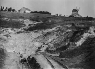 Sandgrube : Blick auf eine Sandgrube mit Schienen. Im Hintergrund ein Gehöft und eine Mühle